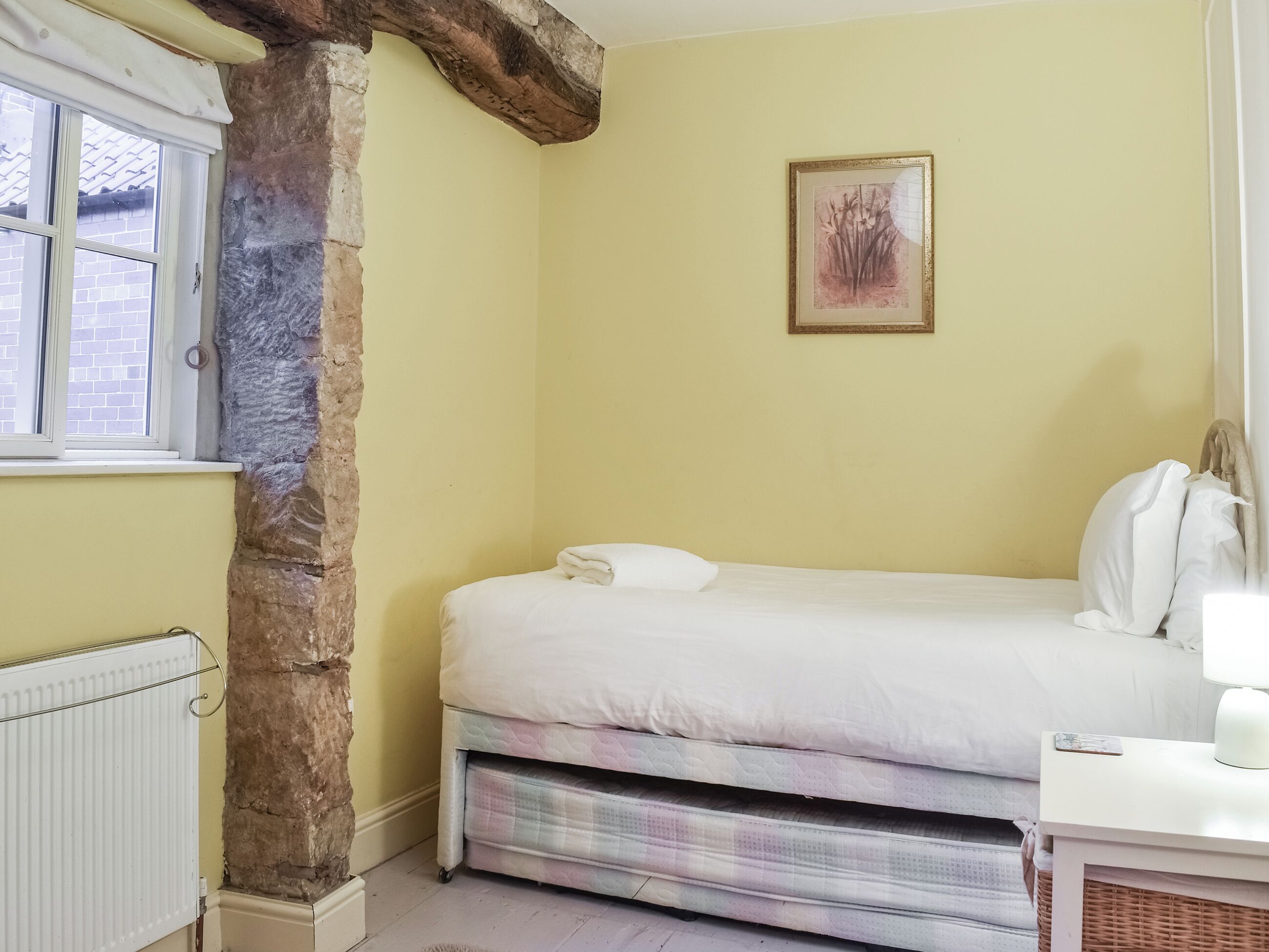 Quarto com uma cama, radiador, um pilar de pedra e uma obra de arte emoldurada na parede.