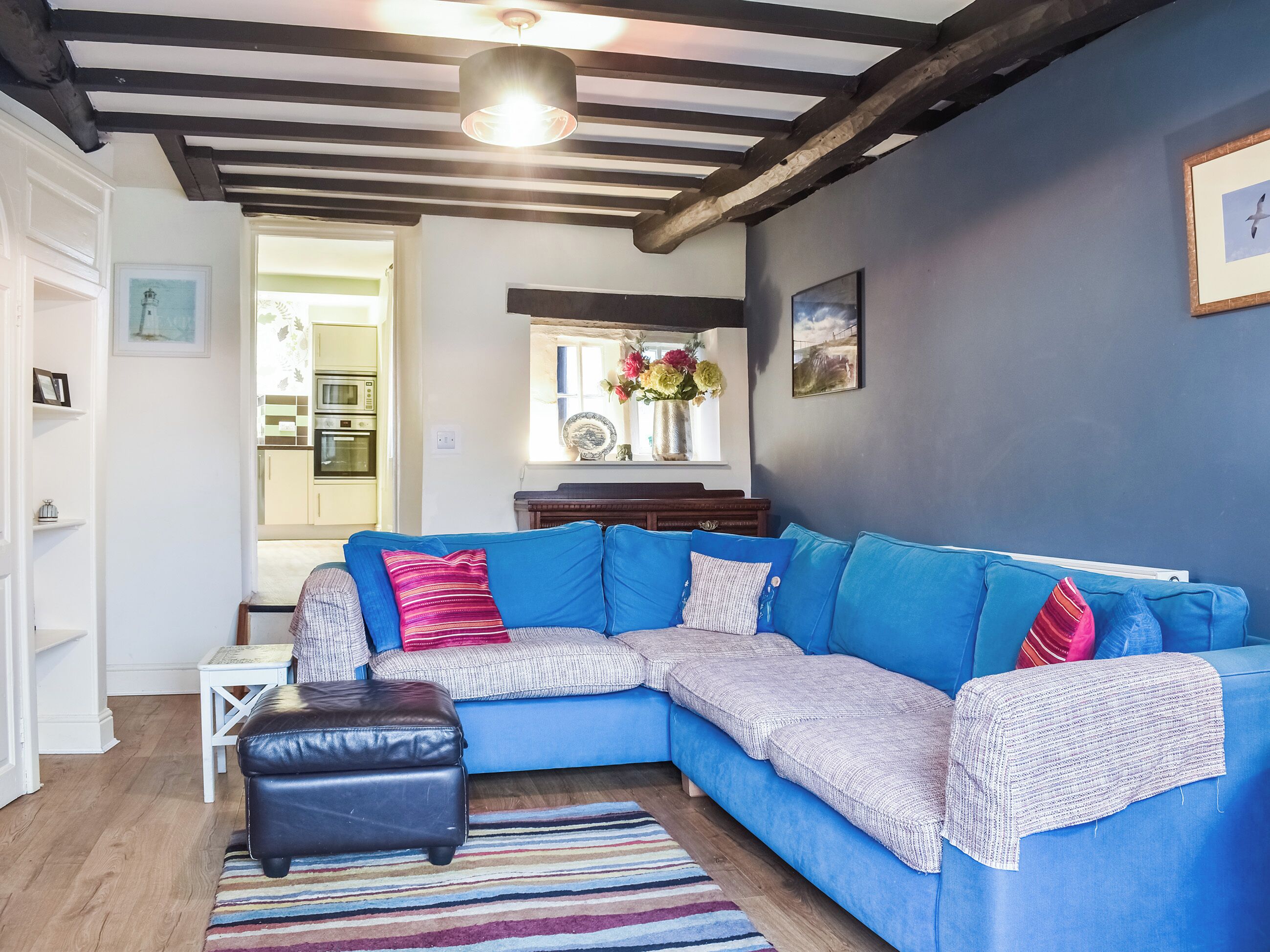 Un salon moderne avec un canapé d’angle bleu, un pouf en cuir noir et un tapis à rayures.