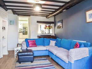 Un salon moderne avec un canapé d’angle bleu, un pouf en cuir noir et un tapis à rayures.