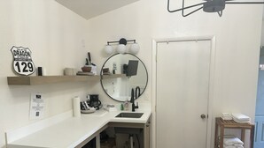 Een compacte keuken met een wit aanrecht, een spoelbak, een spiegel en een klein schap met keukengerei.