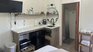 Een compacte hotelkamer met kitchenette, flatscreen televisie, spiegel en klein houten plankje.