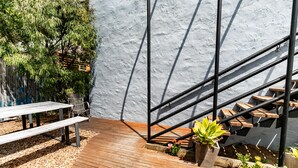 Una terraza de madera con una escalera de metal, una mesa de picnic y plantas en macetas.