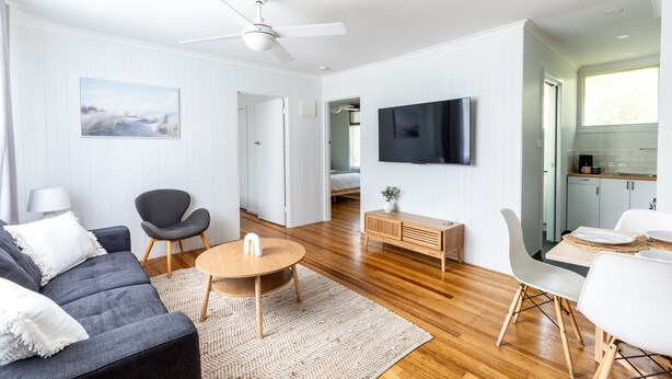 Una sala de estar moderna con sofá, sillón, una mesa redonda y un televisor de pantalla plana montado en la pared.