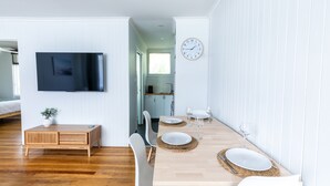 Un comedor moderno con una mesa de madera dispuesta para cuatro, sillas blancas y un televisor montado en la pared.