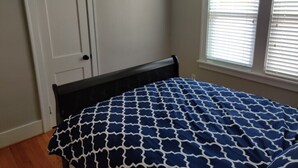 Ein Schlafzimmer mit Bett, Tür und einem Fenster mit Jalousien.