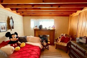A cozy room with a bed, a fireplace, a Mickey Mouse plush toy, and a wooden dresser.