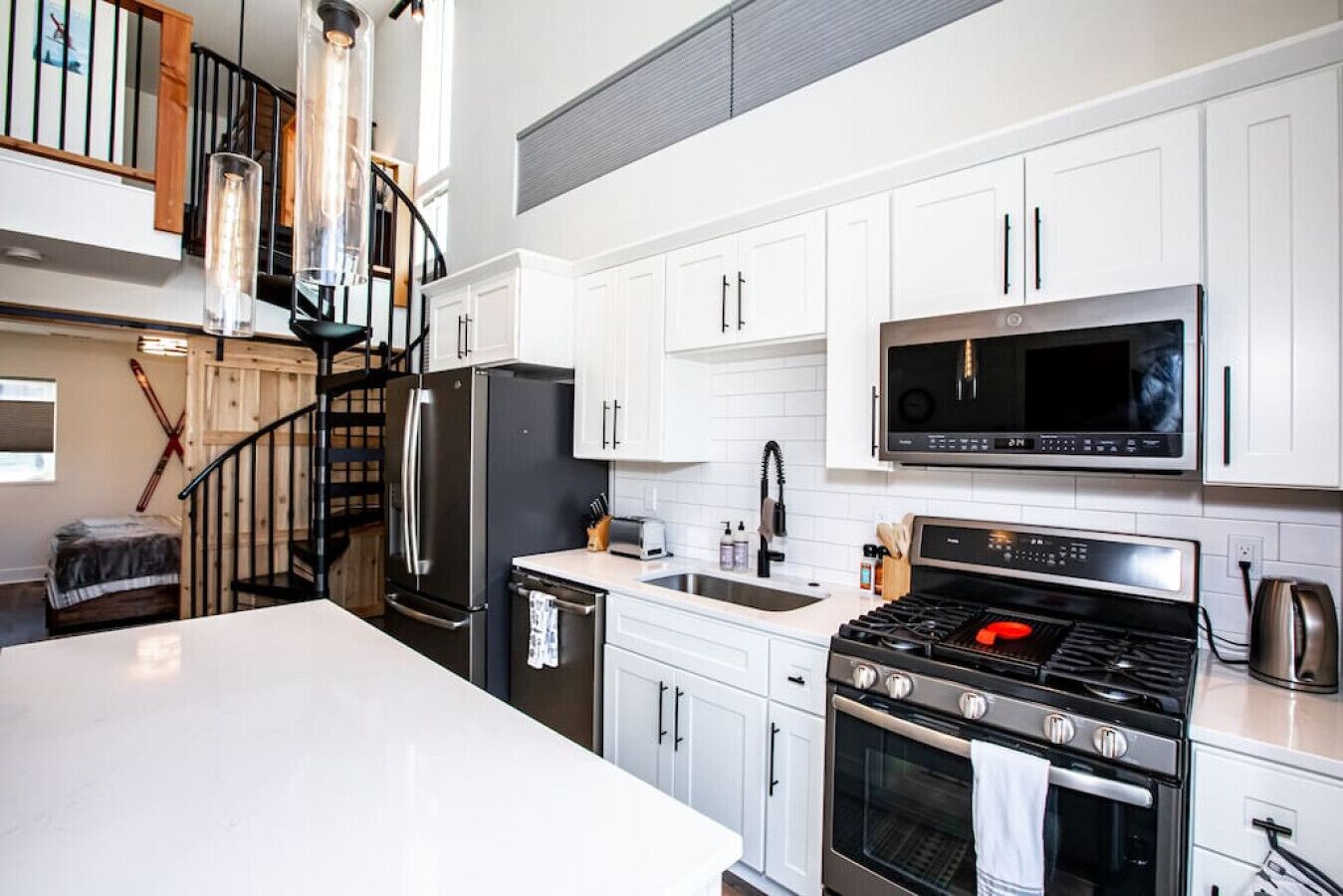 Una cocina moderna con armarios blancos, electrodomésticos de acero inoxidable, un microondas, una estufa y un lavamanos.