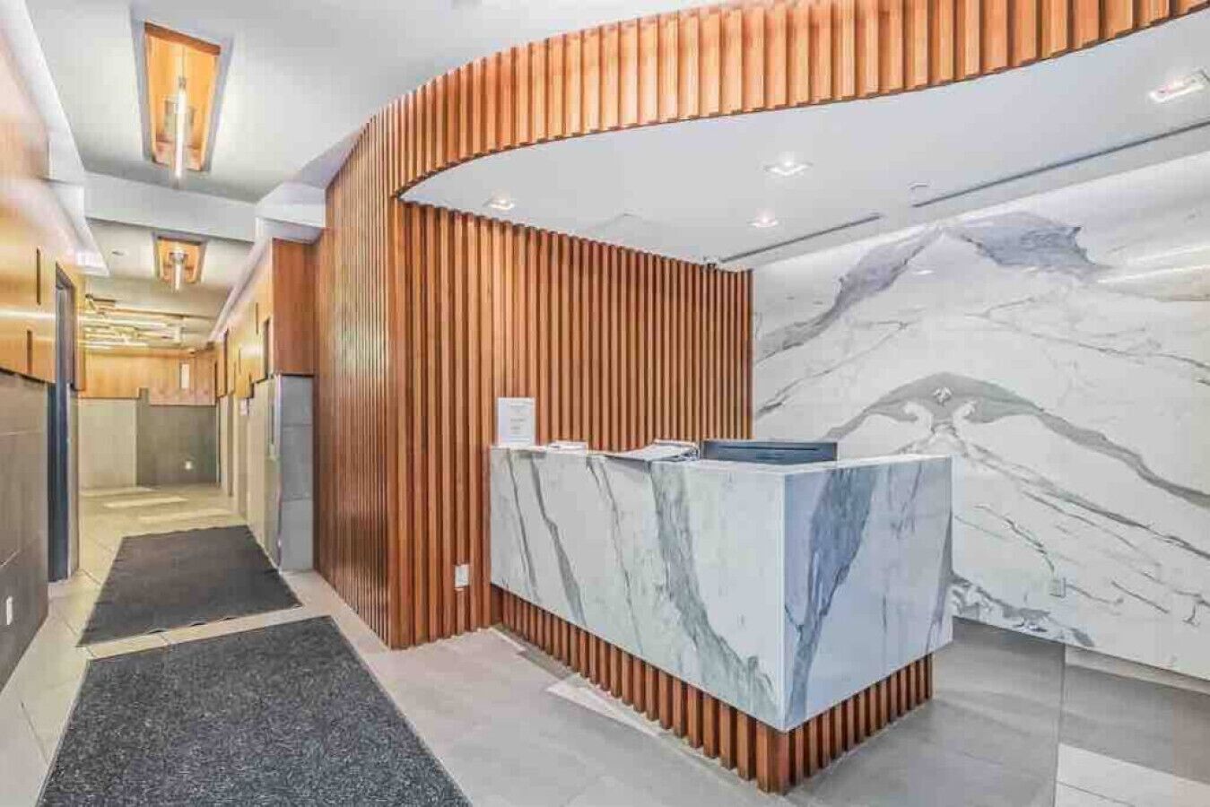 A reception area with a marble counter, wooden paneling, and a corridor leading to elevators.