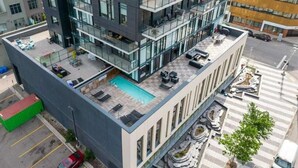 A multi-story building with a rooftop pool area, outdoor seating, and a pedestrian crossing. - Cozy DT Fantastic Amenities View Private Parking (Calgary)