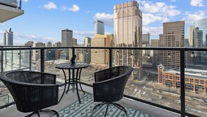 A balcony with two wicker chairs and a small table, overlooking a cityscape with various buildings. - Cozy DT Fantastic Amenities View Private Parking (Calgary)