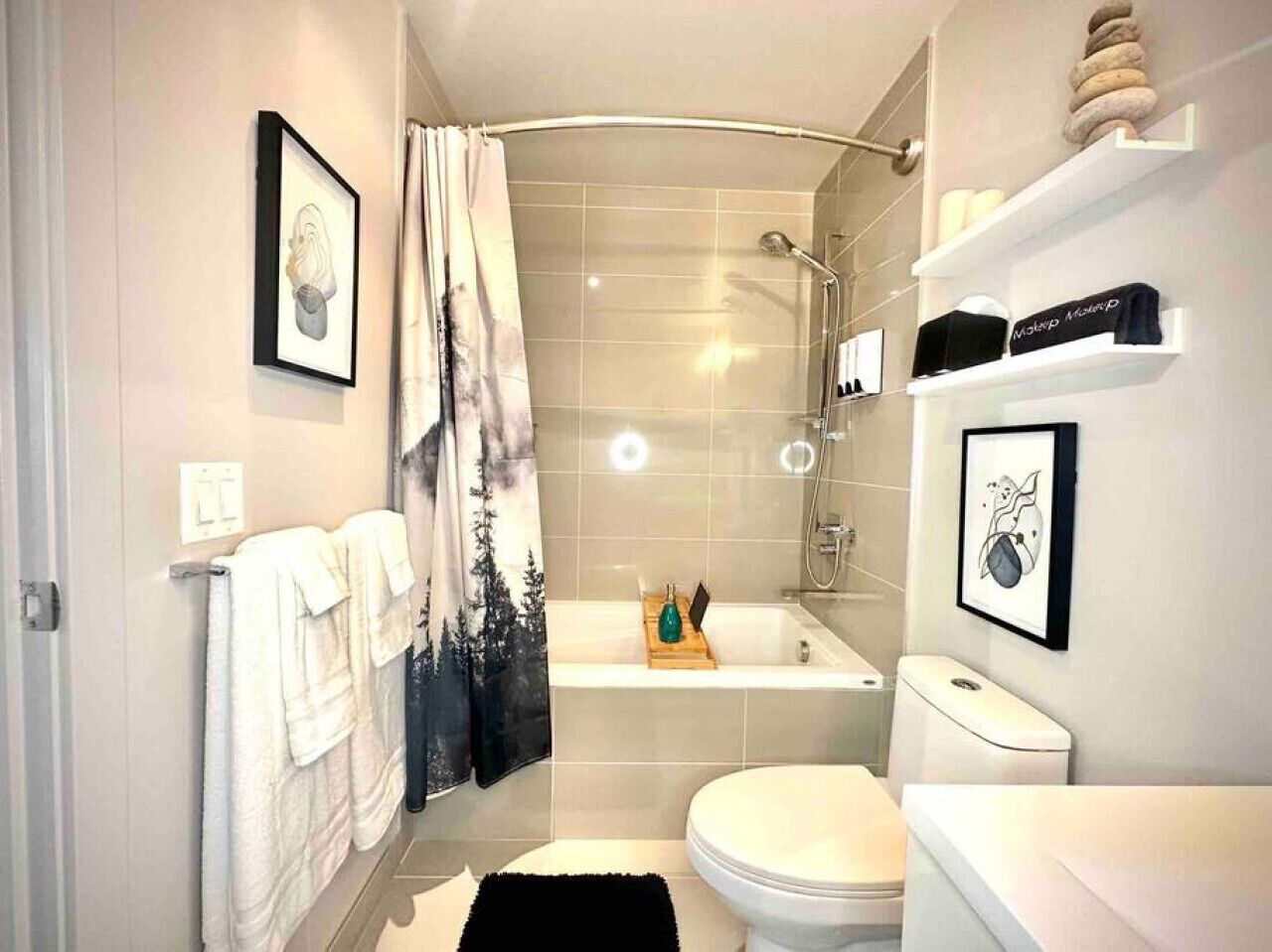 A modern bathroom with a bathtub, toilet, and shower. There are towels on the wall, a framed picture, and a shelf with toiletries.