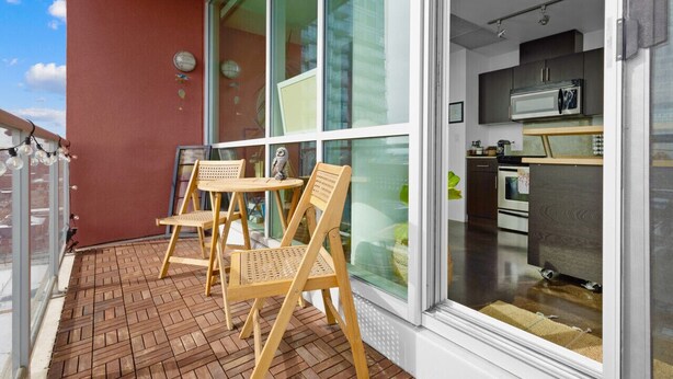 A balcony with wooden chairs and a table, a kitchen with modern appliances, and a red wall. - ColoursNest- Fantastic Location with Amazing Views (Calgary)