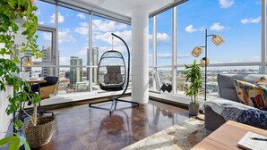 A spacious living room with large windows, a hanging chair, a sofa, and a view of the cityscape. - ColoursNest- Fantastic Location with Amazing Views (Calgary)