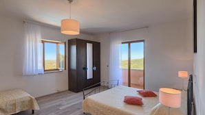 Ein Schlafzimmer mit Bett, Schreibtisch, Stuhl, Kleiderschrank und einem Balkon mit Blick.