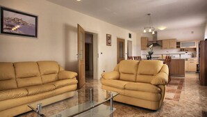 Ein großzügiger Wohnbereich mit zwei beigen Sofas, einem Glastisch und einer Küche im Hintergrund.