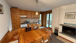 A kitchen with wooden cabinets, a dining table, chairs, a stove, and a fireplace. - Crêtes X2 232 - SUNNY apartment 6 pers (Veysonnaz)