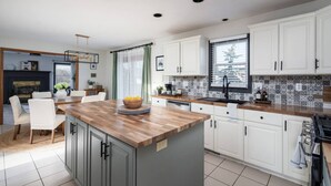 A modern kitchen with white cabinets, a wooden island, and a tiled backsplash. - `Corporate Elegance: Luxe Home in Grand Rapids` (Kentwood)