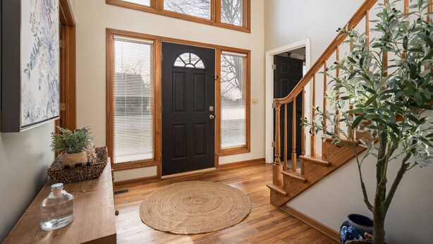 A spacious entryway with a wooden staircase, a black door, and a large potted plant. - `Corporate Elegance: Luxe Home in Grand Rapids` (Kentwood)