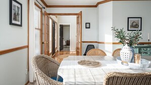 A dining area with a wooden table, wicker chairs, a vase with flowers, and a framed picture on the wall. - `Corporate Elegance: Luxe Home in Grand Rapids` (Kentwood)