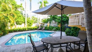 A pool area with a round table and chairs, surrounded by greenery and a white fence. - Waterfront Condo Near Las Olas and Beach (Fort Lauderdale)