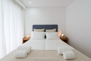 A neatly made bed with white linens and two pillows, flanked by bedside tables with lamps.