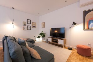 A modern living room with a grey sofa, a flat-screen TV, a floor lamp, and framed pictures on the wall.