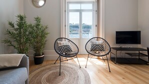 Una sala de estar con dos sillones, un sofá, un televisor, una planta en maceta y vistas a través de un amplio ventanal.