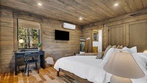 Ein Schlafzimmer mit Holzboden, einem Bett mit weißer Bettwäsche, einem Schreibtisch mit Stuhl und einem an der Wand befestigten Fernseher.
