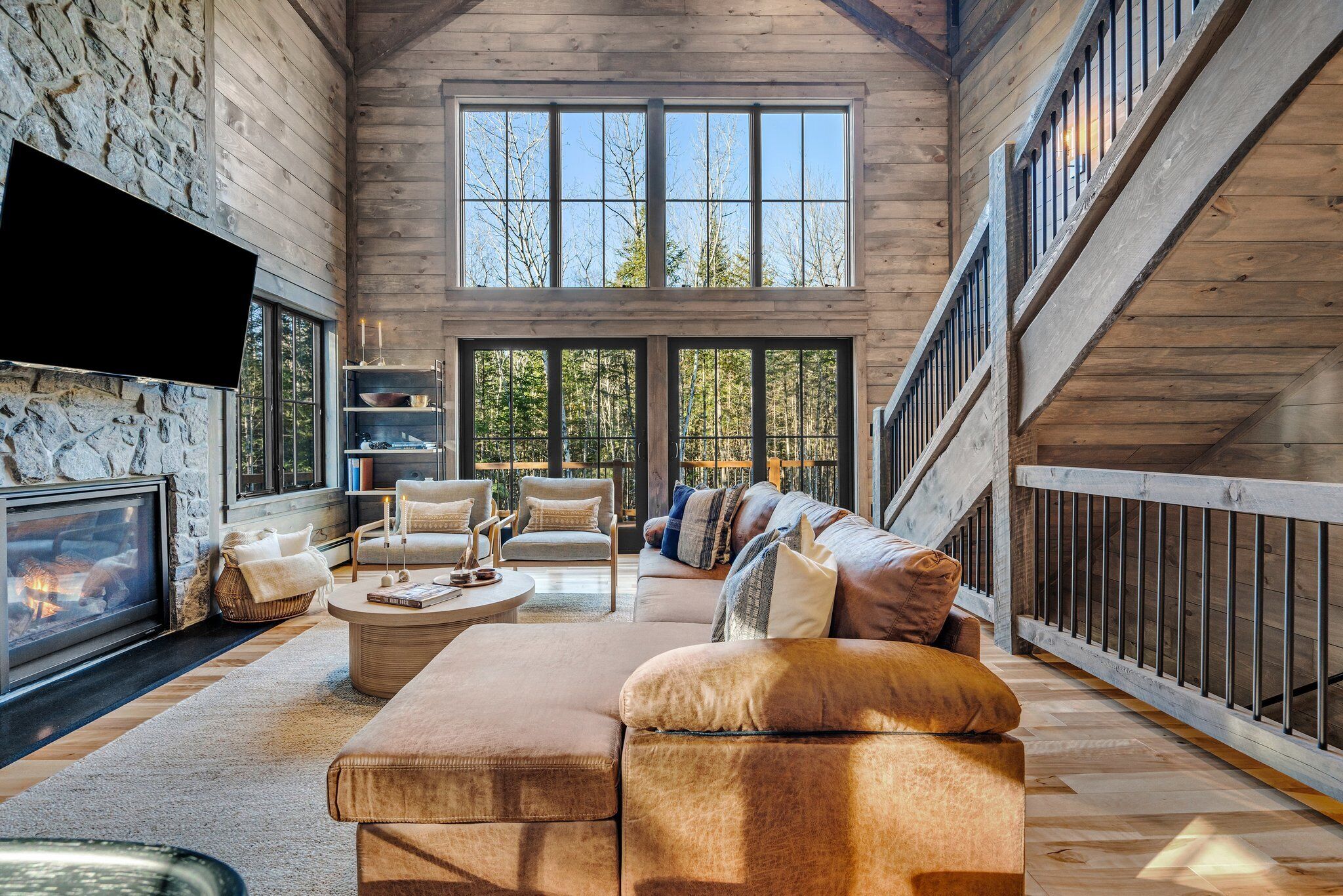 A spacious living room with a fireplace, comfortable seating, and large windows offering a view of the outdoors.
