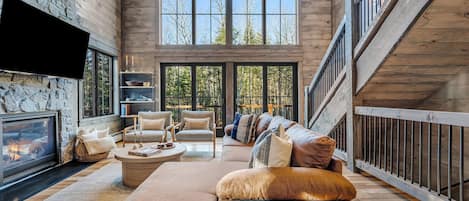 A spacious living room with a fireplace, comfortable seating, and large windows offering a view of the outdoors.
