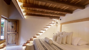 A bedroom with a large bed, a wooden staircase, and a wooden door.