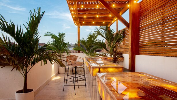 A rooftop bar with a wooden pergola, seating, and potted plants.