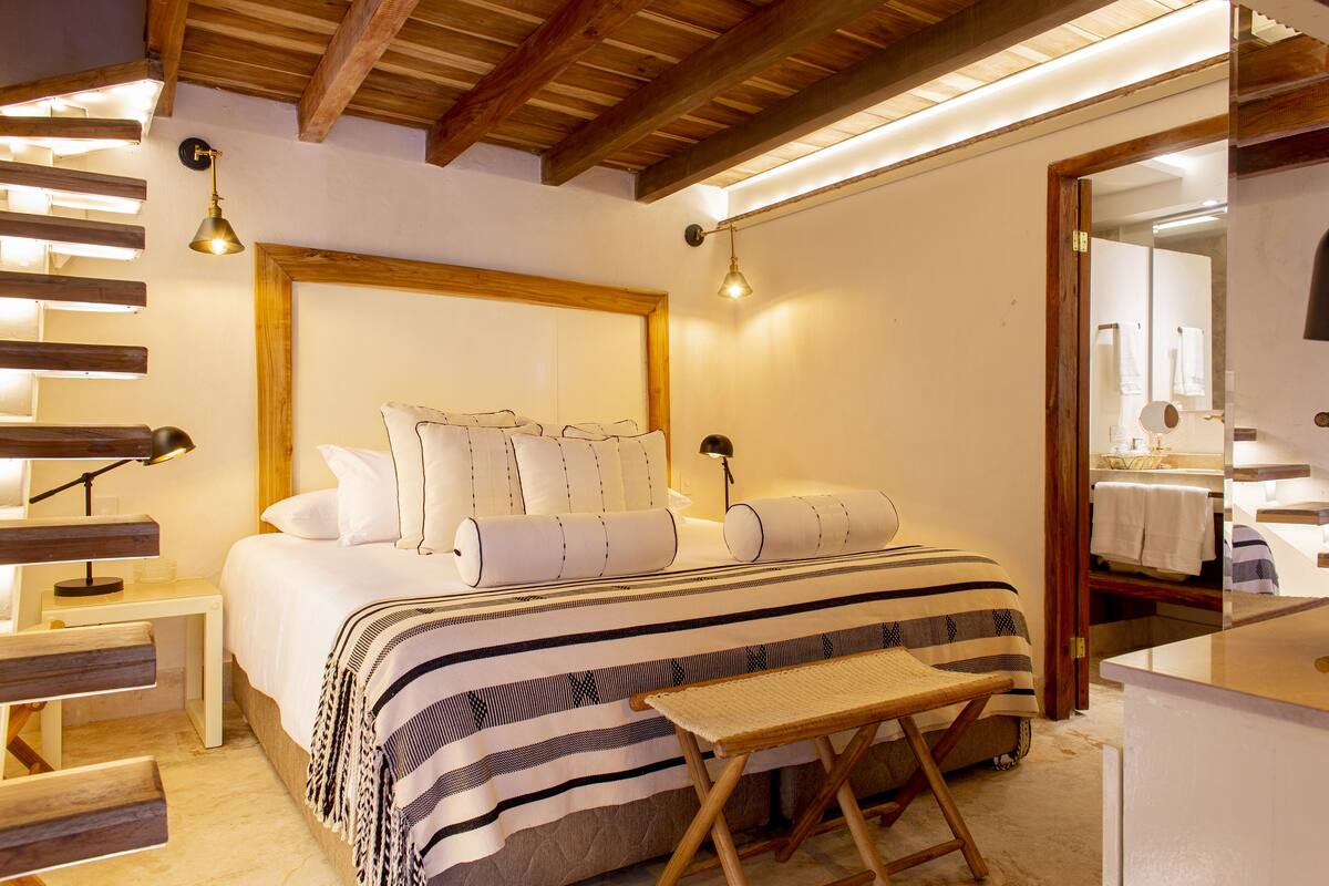 A bedroom with a large bed, bedside tables, a bench, and a mirror.