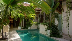 A pool area with a tiled floor, surrounded by potted plants and a building with a tiled roof.