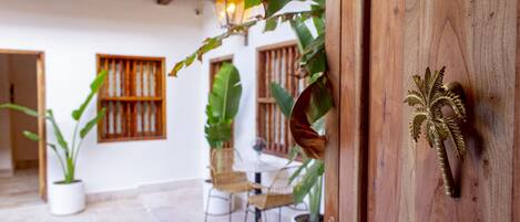 A wooden door with a decorative brass handle, a potted plant, and a dining area with chairs and a table.