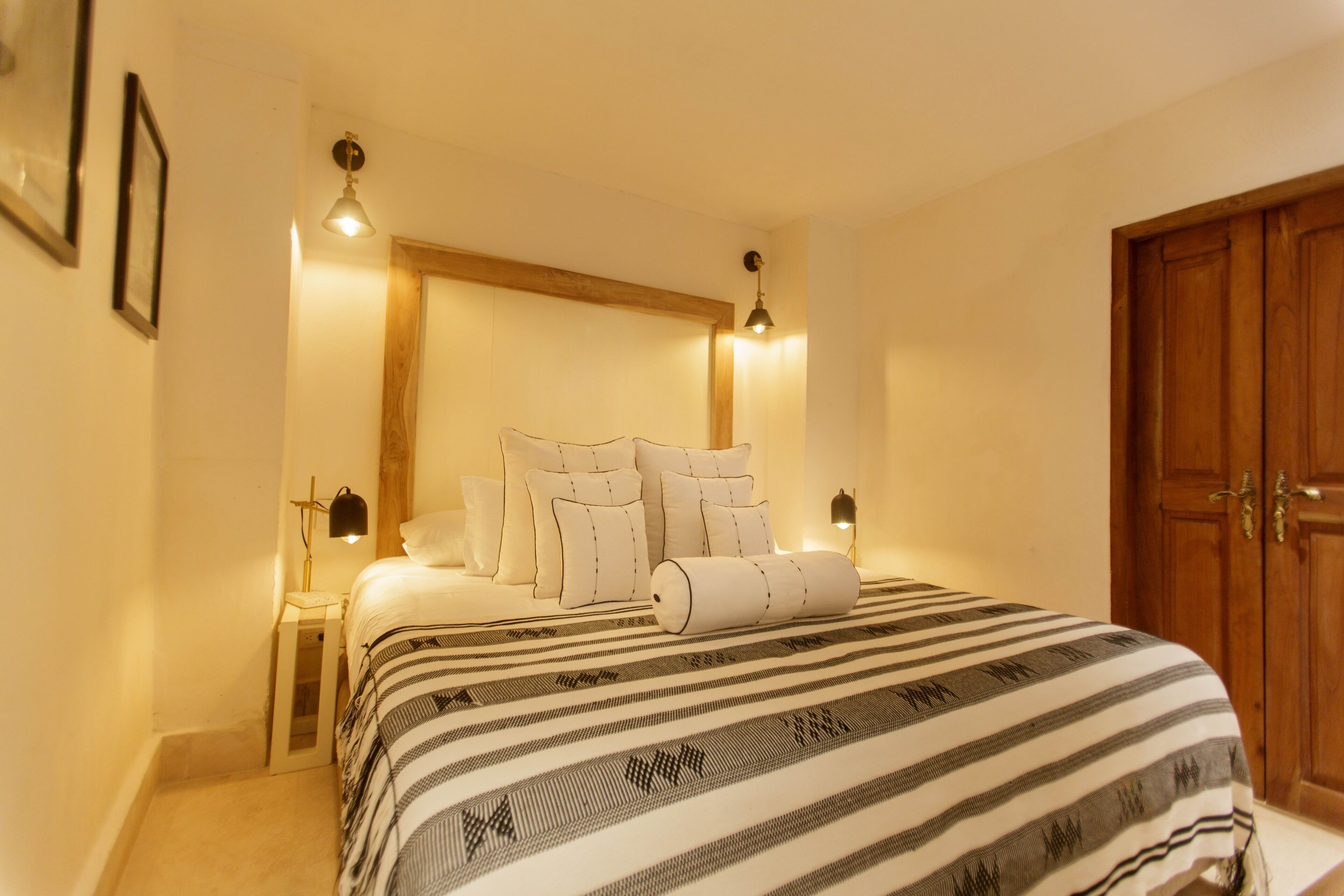 Un lit bien fait, avec une couvre-lit à rayures, deux lampes de chevet et une tête de lit en bois.
