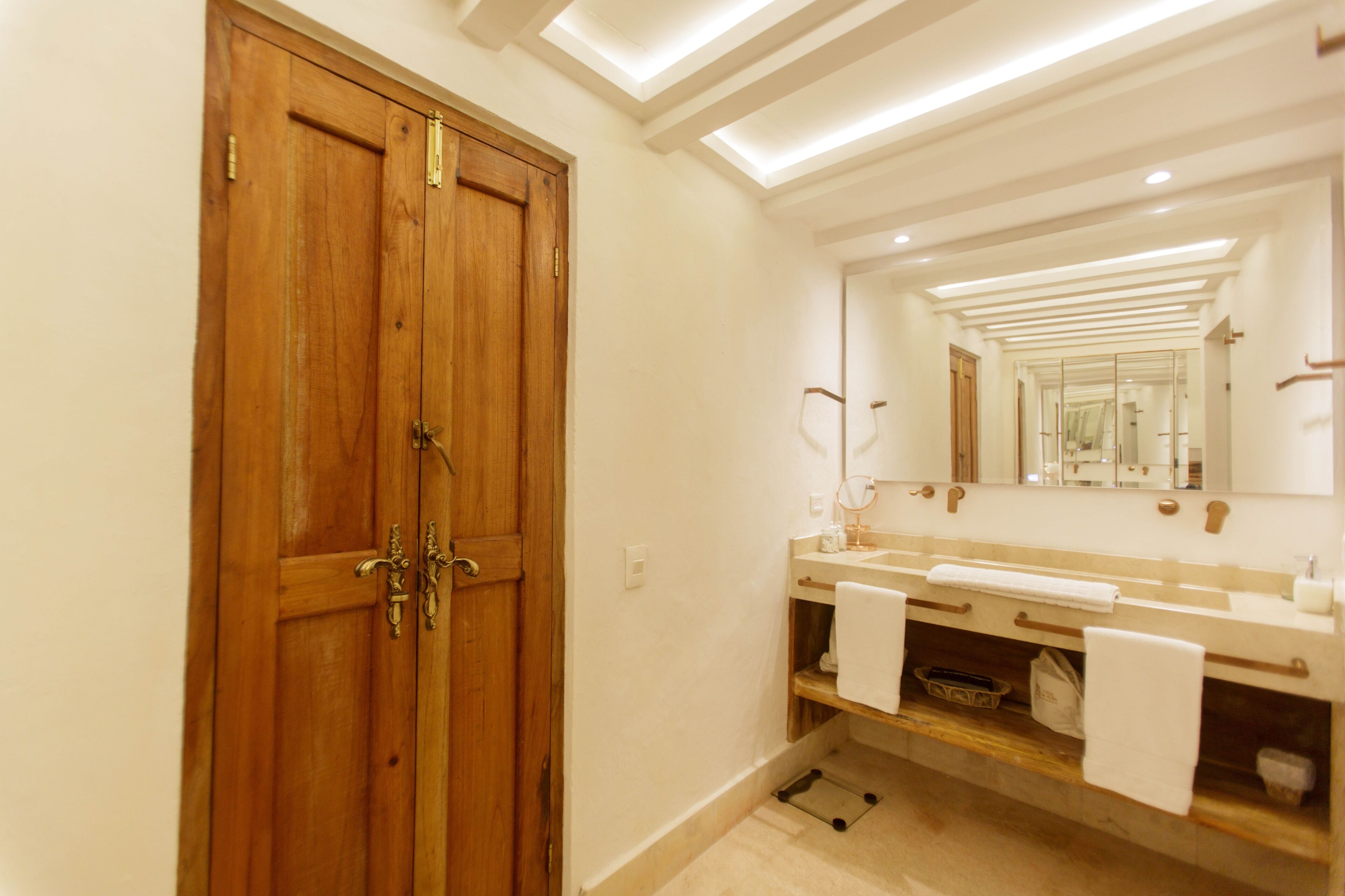 A bathroom with a wooden door, a sink with a mirror, and a towel rack.