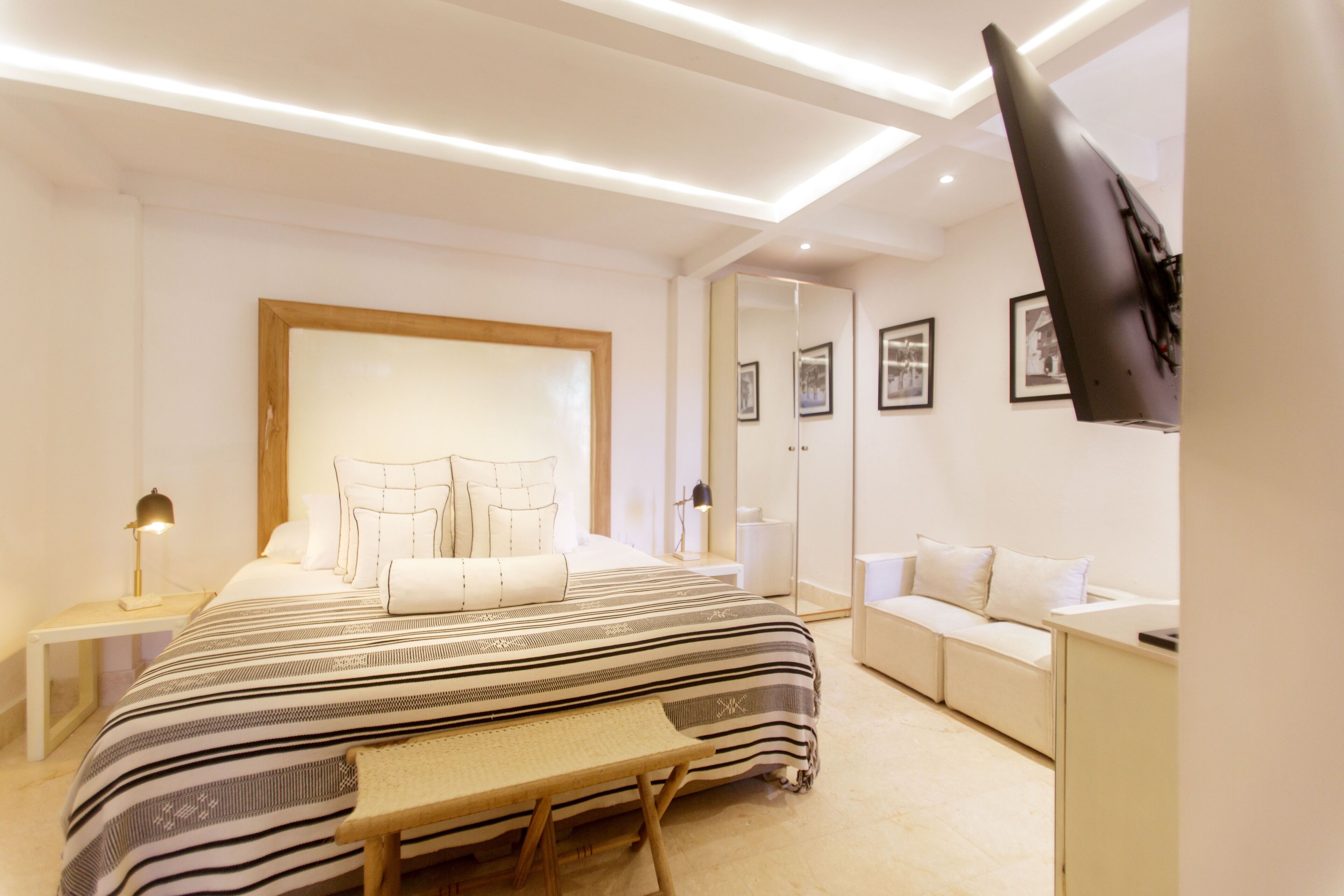 A modern bedroom with a large bed, bedside tables, a desk, and a TV mounted on the wall.