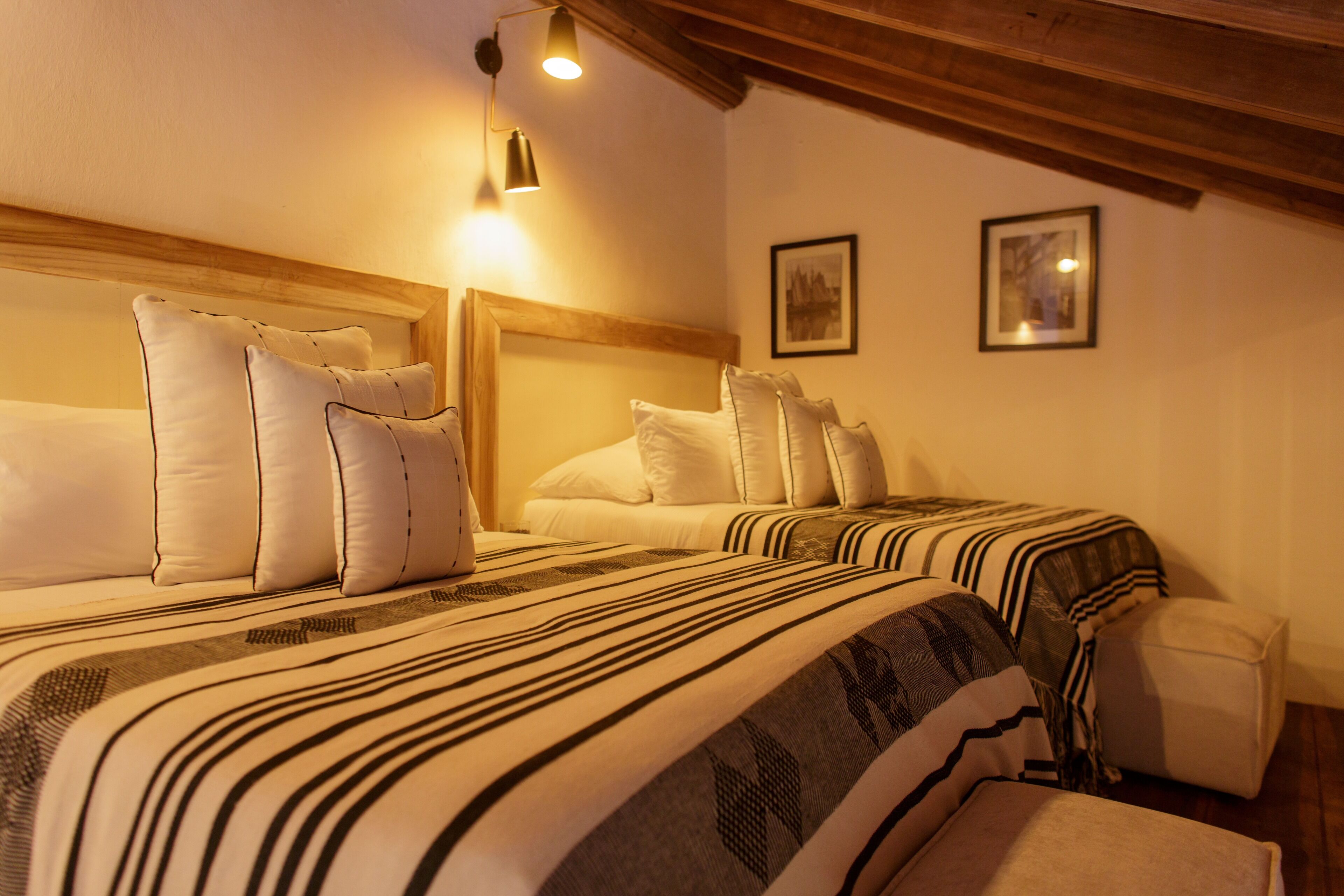 Ein Hotelzimmer mit zwei Betten, beide mit gestreifter Bettwäsche und Kissen. An der Wand befinden sich zwei gerahmte Bilder.