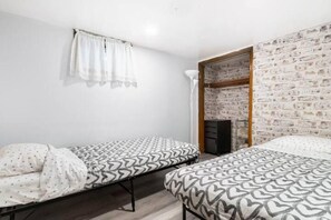 A room with two single beds, a white curtain, a brick-patterned wall, and a white floor lamp. - Never overpay, 19 min to NYC, minutes to NYC (Newark)