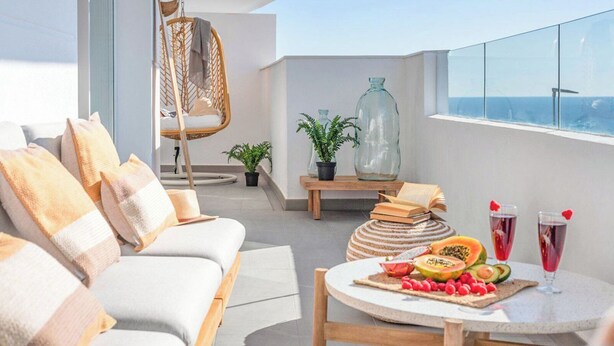 A modern outdoor seating area with a sofa, a hanging chair, and a round table with fruit and drinks. - Apartamento Balcón Rincón de la Victoria by Ruralidays (Málaga)