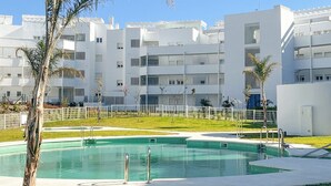 A modern building with a swimming pool surrounded by a fenced area and palm trees. - Apartamento Balcón Rincón de la Victoria by Ruralidays (Málaga)