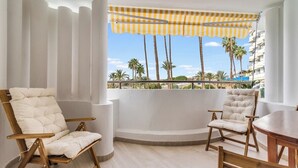 A balcony with two cushioned chairs and a wooden table, overlooking palm trees and a clear sky. - Home2Book Design Apartment Maspalomas Paraíso (Maspalomas)