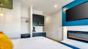 Une chambre d’hôtel moderne équipée d’un lit, d’un téléviseur à écran plat fixé au mur, d’une cheminée intégrée et d’un coin cuisine.