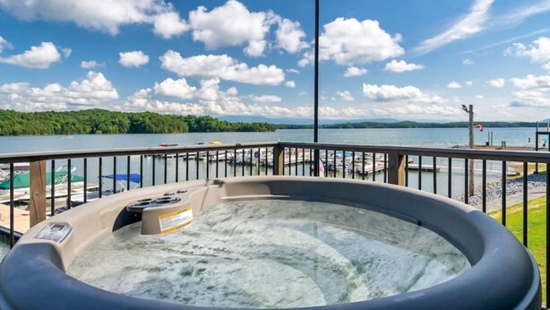 Een hottub op een terras met uitzicht op een meer en aangemeerde boten.