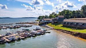 A marina with boats docked, a grassy area with buildings, and a body of water with a distant shoreline.