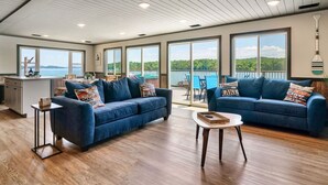 A spacious living area with two sofas, a coffee table, and a kitchen area with a view of the outdoors.