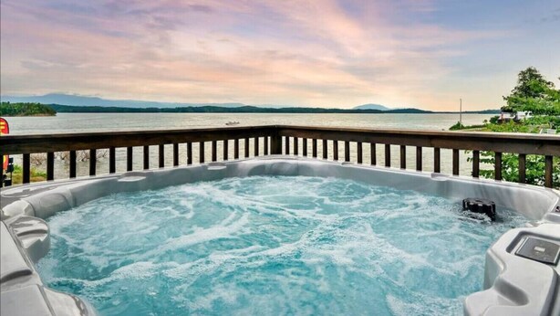 Een hottub met een houten terras en uitzicht op een meer en bergen.