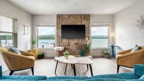 Een woonkamer met een stenen open haard, een flatscreen televisie, twee fauteuils, een bank en uitzicht op het water.