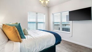 Een slaapkamer met een bed, een aan de muur bevestigde televisie en ramen met zonwering.
